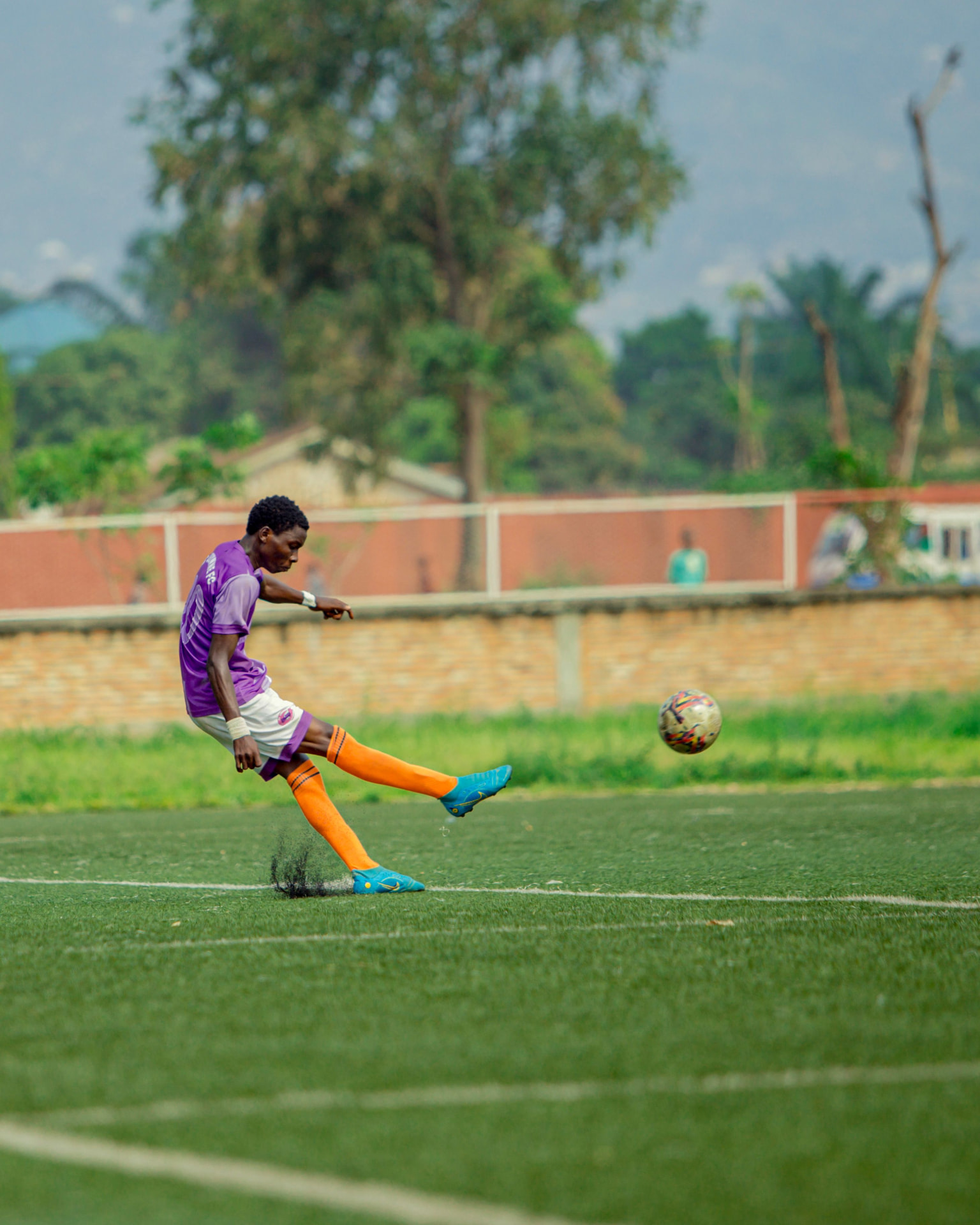 Footballer in purple kit striking a long ball