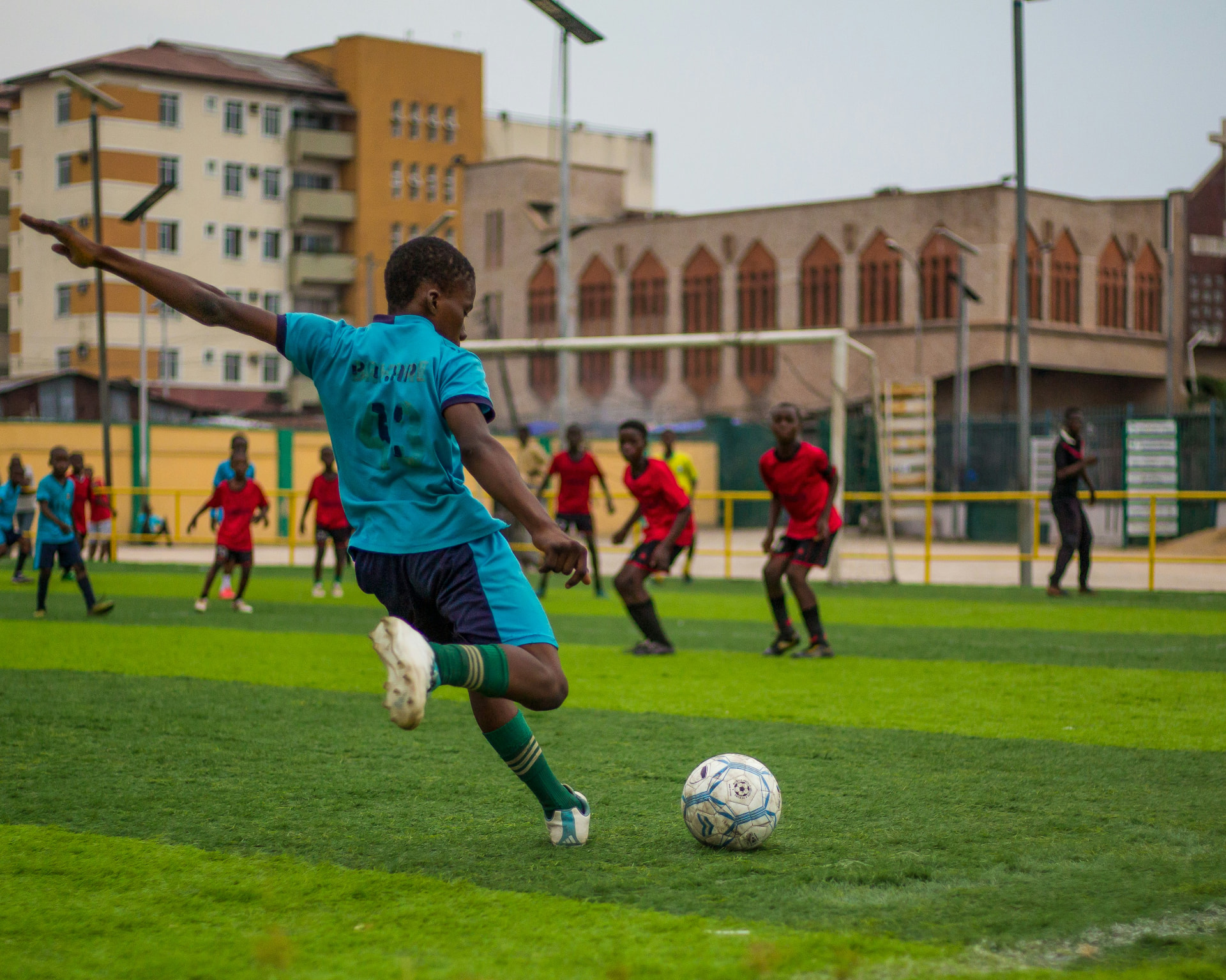 Young footballer in blue kit striking the ball on an urban pitch